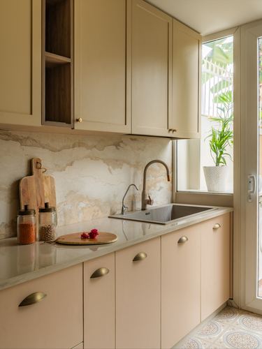 Cream and blush kitchen with stone backsplash, brass handles, and window with plant