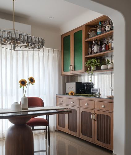 Dining nook with sunflower vase beside a wood bar unit with green leather cabinet doors and glass shelves of bottles