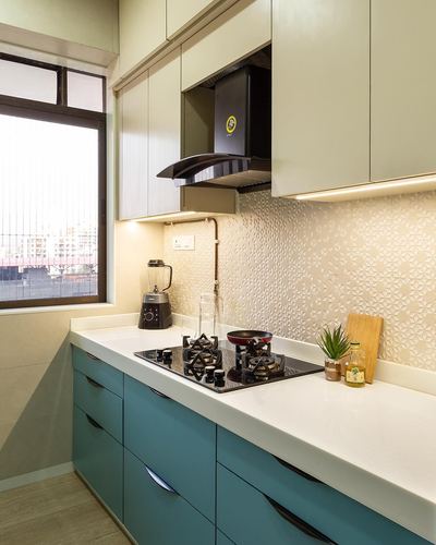 Modular kitchen corner with teal cabinets, black hob, and textured cream backsplash under a window