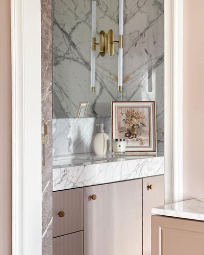 Pink ribbed vanity with marble countertop, mirror wall, and brass sconce with candle sticks