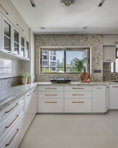 White L-shaped kitchen with patterned stone backsplash and city-view window