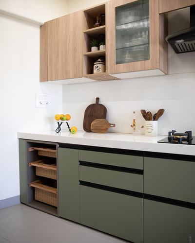 Modern kitchen with olive-green base cabinets, wood upper units, white countertop and wicker pull-out baskets