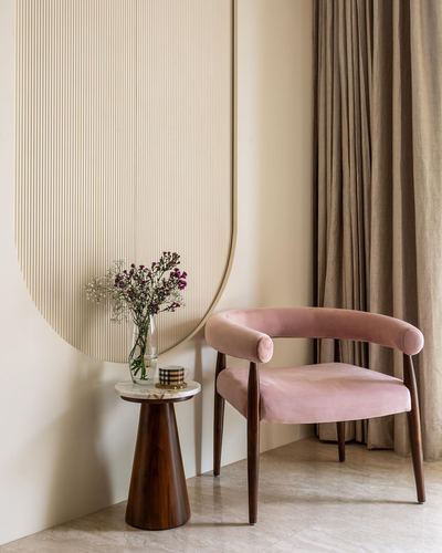 Pink velvet curved armchair beside marble-top side table under an oversized fluted arch mirror