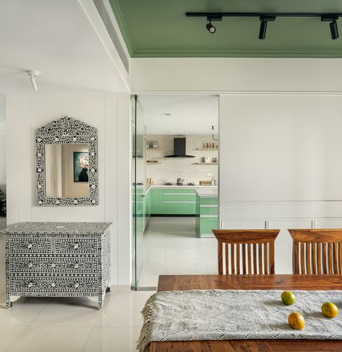 Dining area with bone inlay mirror and chest, sage green ceiling cove, view into green kitchen beyond