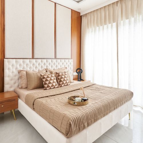 Beige tufted bed against wood-paneled wall with sheer curtains and brass tray styling