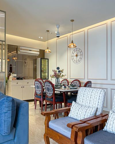 Dining area with round table, patterned chairs, pendant lights and paneled wall clock, kitchen visible beyond
