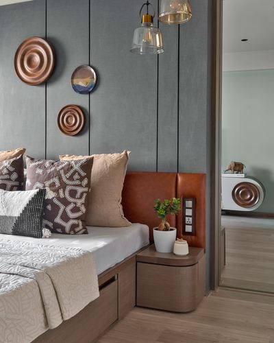 Bedroom corner with grey paneled wall, copper wall plates, tan leather headboard, and layered cushions