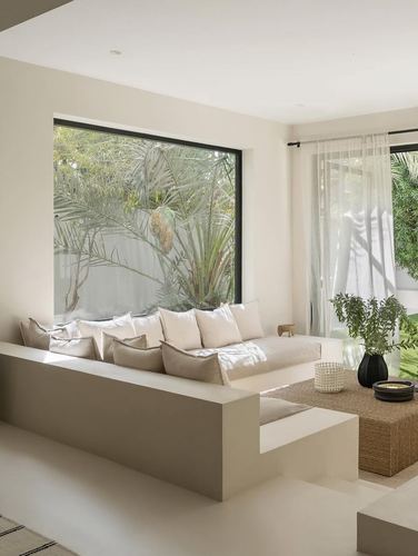 Sunken plaster banquette with linen cushions facing large window onto green garden