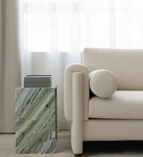 Cream boucle sofa with round bolster beside a green marble side table near sheer curtains