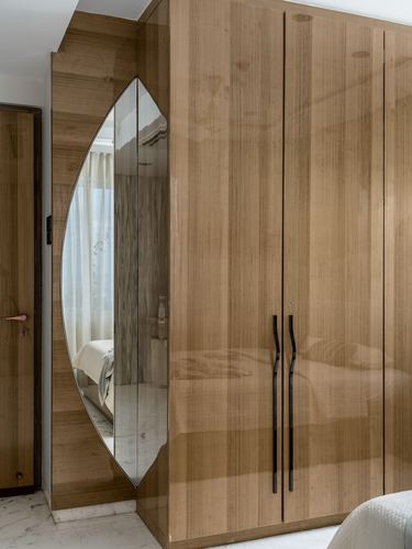 Leaf-shaped mirror set into glossy wood wardrobe reflecting a bed in soft light