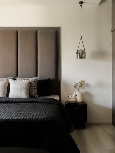 Bedroom with tall channel-tufted brown headboard, black bedding, and a glass pendant light beside a dark nightstand.
