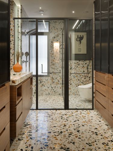 Bathroom with terrazzo floor and walls, glass shower partition, walnut vanity, and wall-mounted toilet beyond