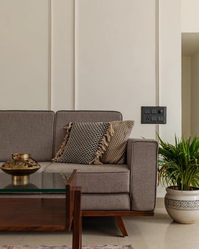 Grey sofa with patterned cushions against panelled wall, wooden coffee table and potted plant beside it