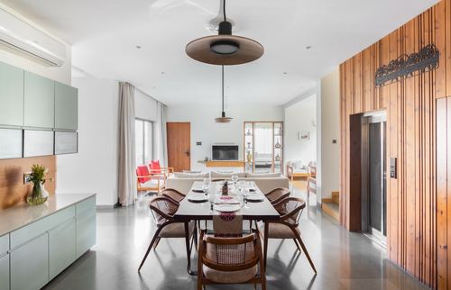 Open dining and living area with cane chairs, pendant lights, and a wood-slat wall hiding an elevator
