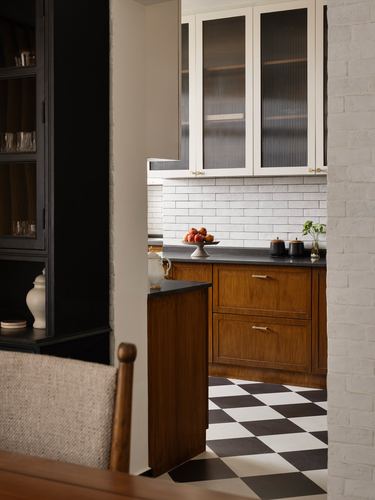View through a brick archway into a wood kitchen with checkerboard floor and ribbed glass cabinets