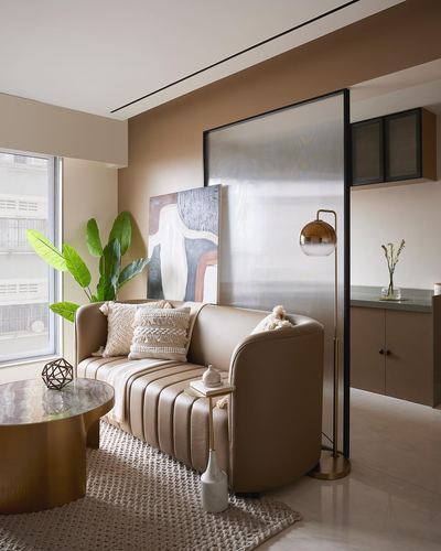Curved taupe leather sofa beside brass floor lamp and reeded glass partition in a warm-toned living room