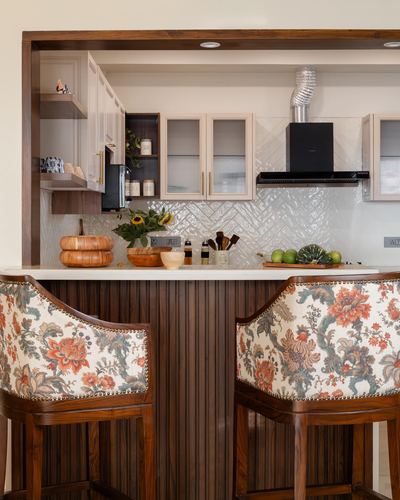 Kitchen pass-through with textured white backsplash, wooden cabinetry, and floral-upholstered bar stools