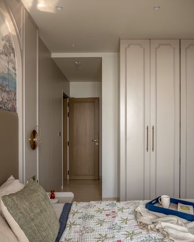 Bedroom corner with paneled wardrobe, wooden door to hallway, and floral quilted bed with breakfast tray