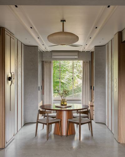 Symmetrical dining nook with round wooden table facing a window view of palm leaves