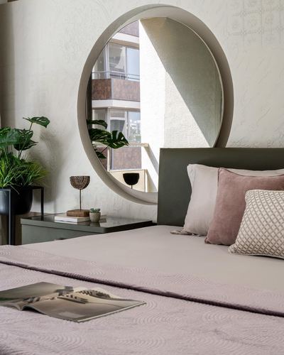 Bedroom corner with round mirror above green headboard, pink pillows, and bedside plant