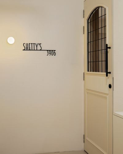 Entry corridor with textured white wall, sconce, name plaque, and arched paneled door