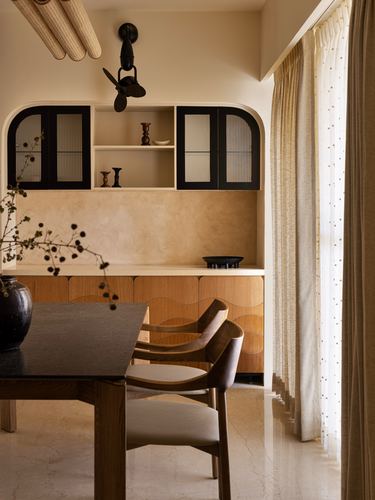 Dining nook with arched black cabinets, wood table, curved wood drawers, sheer dotted curtains