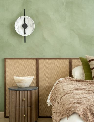 Sage green bedroom corner with cane headboard, fluted wood nightstand, marble clock and knit throw