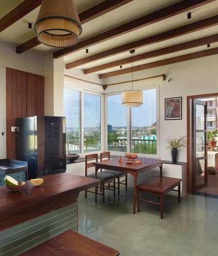 Dining nook with wooden table, bench and cane pendant lights beside corner windows overlooking city view