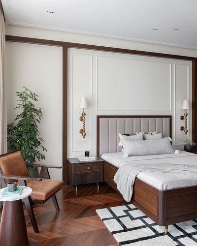 Bedroom with channel-tufted headboard, wood-trimmed paneling, herringbone floor and leather armchair