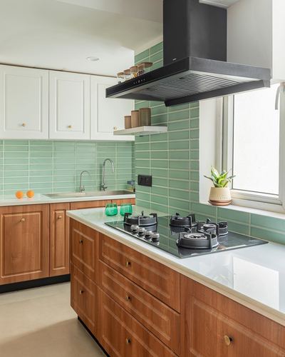 Kitchen island with wood cabinetry, black chimney hood, and green tiled backsplash
