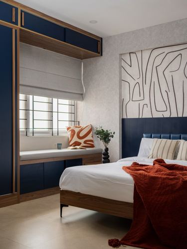 Bedroom with navy cabinetry, window seat, textured wall panel and rust throw on bed