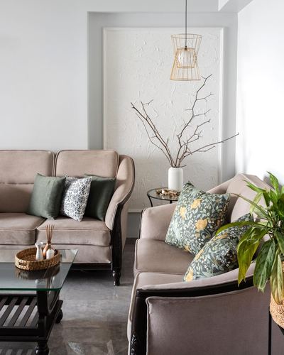 Beige sofas with green floral cushions face a textured white art panel and wire pendant light