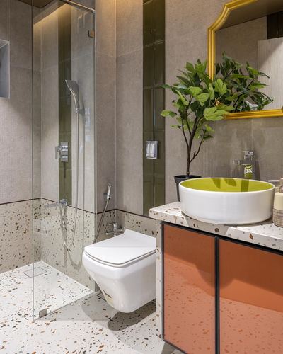 Bathroom with terrazzo floor, glass shower, green sink and orange cabinet, gold mirror
