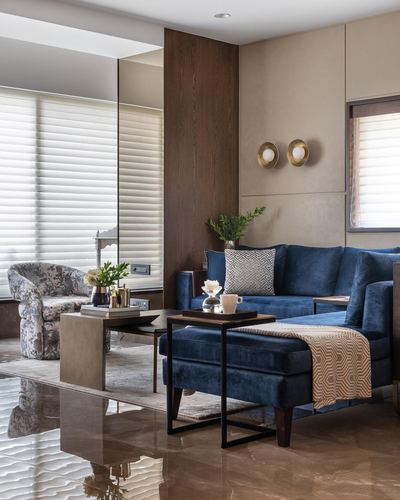 Living room with navy velvet sectional, brass sconces, wood panelling and reflective marble floor