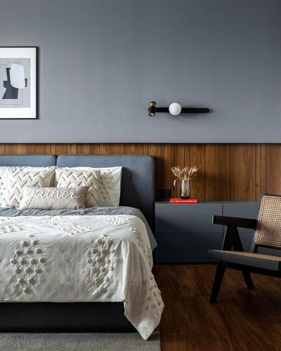 Grey bedroom with wood wainscoting, upholstered bed, and cane accent chair