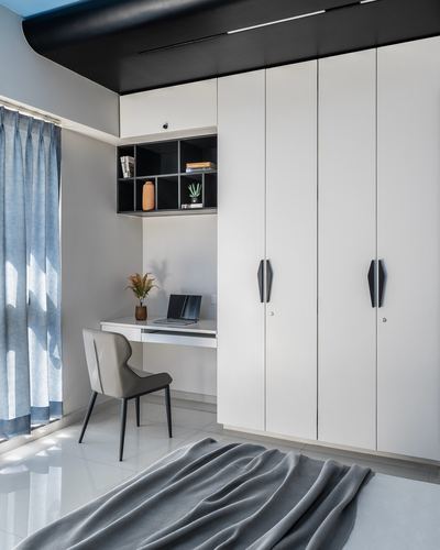 Minimalist study nook with white wardrobe wall, black open shelving, small desk and grey chair by curtained window