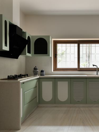 Sage green L-shaped kitchen with arched cabinet cutouts, black chimney hood, and wooden grilled window
