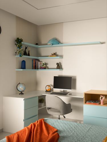 Corner study nook with pale blue floating shelves, white L-shaped desk, computer, and globe beside a bed with orange throw.