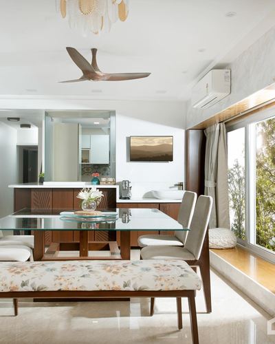 Dining area with glass table, floral bench, and window seat overlooking greenery