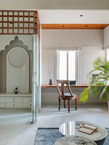 Living space with carved arched mandir niche, wooden lattice screen, study desk and round marble table