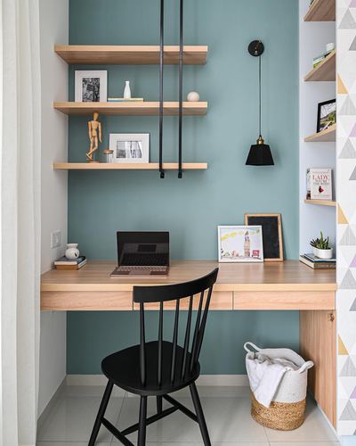 Compact study nook with teal wall, floating wood shelves, desk, black chair and pendant light