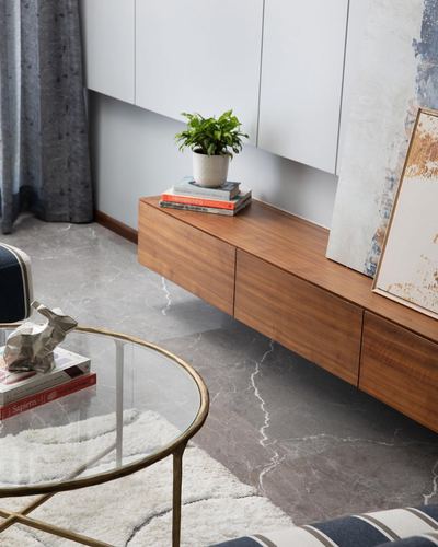 Floating wood console with plant and books beside a glass coffee table on grey marble floor