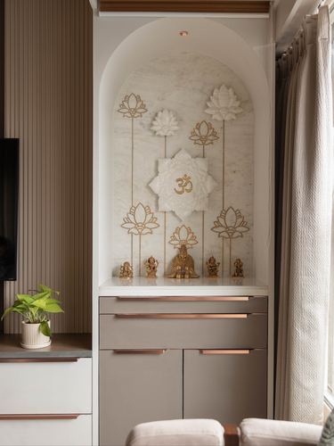 Arched pooja niche with lotus reliefs, om symbol, and brass idols above taupe cabinetry