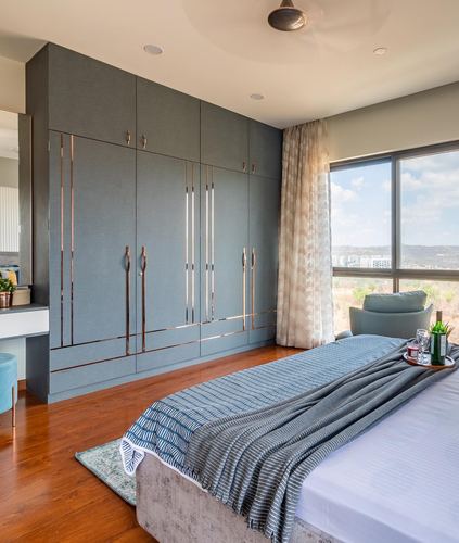 Bedroom with grey wardrobe featuring metallic inlay strips, wooden floor, and city view through window