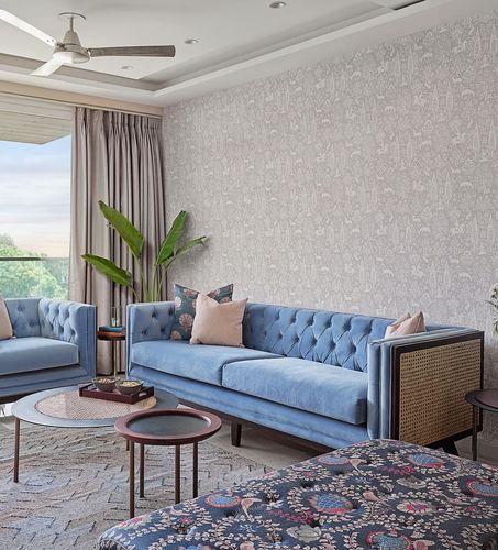 Blue tufted sofa with cane side panel against patterned wallpaper, balcony view beyond