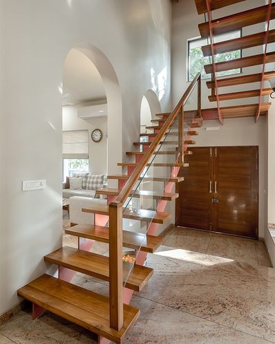Wooden staircase with pink risers and glass railing beside an arched doorway to living room