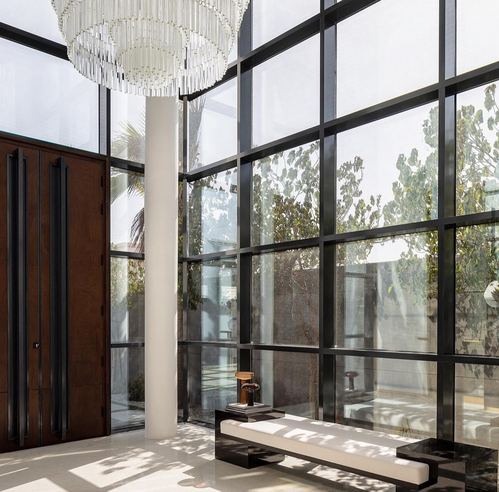 Double-height entry foyer with crystal chandelier, glass wall, wooden door and marble floor