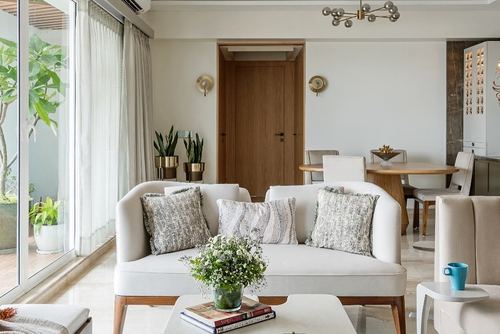 Neutral living room with curved white sofa, wooden door, and dining area beyond