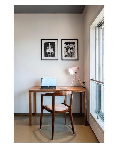Wooden desk and curved wood chair beside a window, two framed prints above