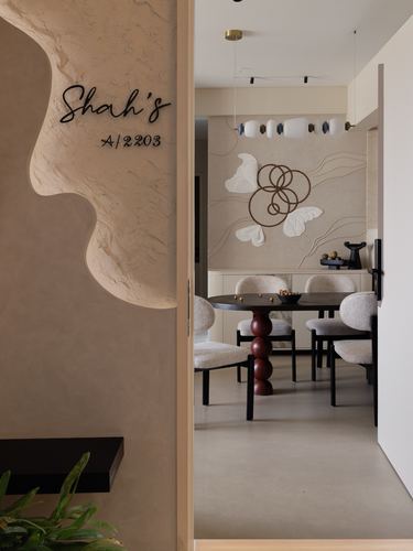 Entry foyer with sculpted plaster wall reading 'Shah's A/2203', opening into a dining room with sculptural pendant light